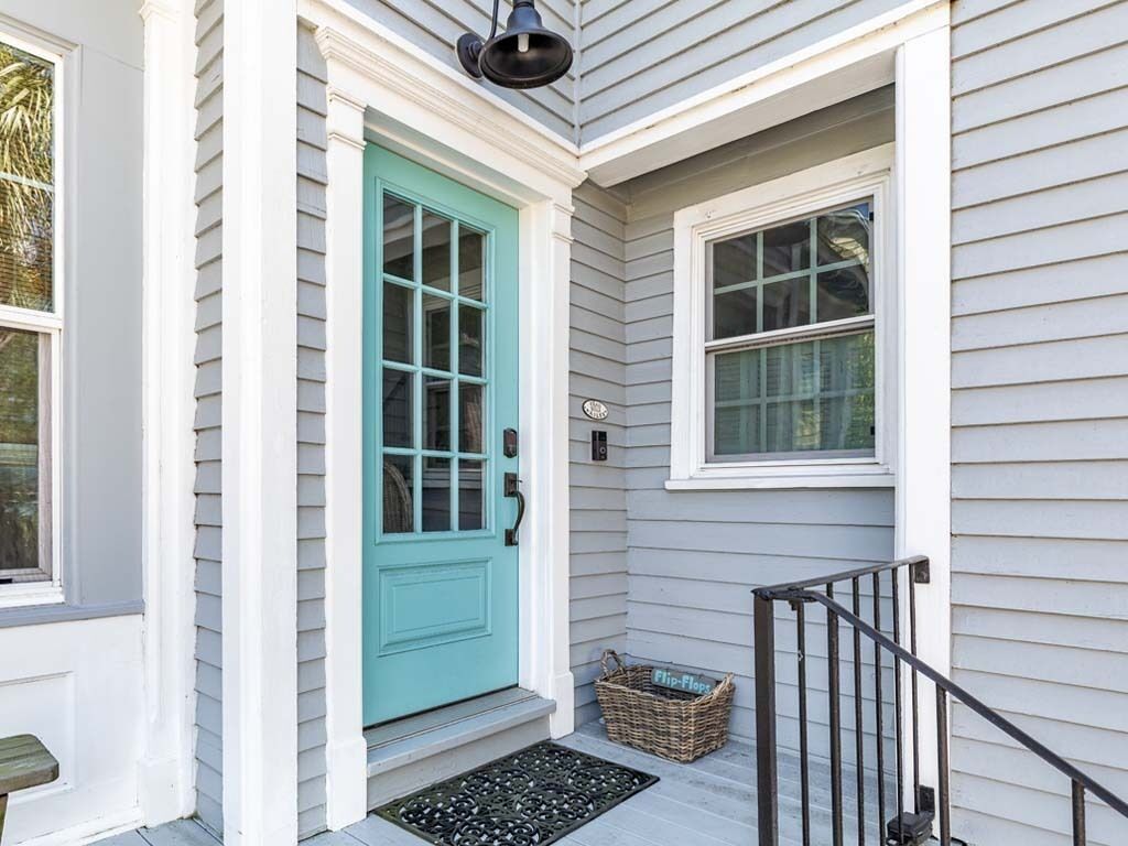 A house with a turquoise front door, a small porch with a black metal railing, and a wicker basket labeled "Flip-Flops" on the steps.