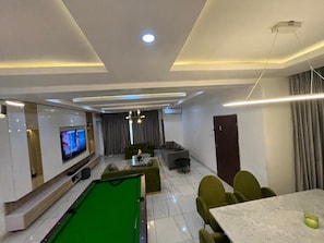 Uma sala de estar moderna com mesa de bilhar, televisão e área de estar com sofá e poltronas.