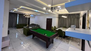 Een moderne woonkamer met een pooltafel, groene banken en een eethoek met een tafel en stoelen.