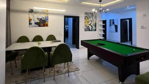 Een moderne eetruimte met een pooltafel, groene stoelen en een marmeren vloer.