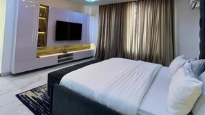 Een moderne slaapkamer met een groot bed, een tv die aan een wit meubelstuk is bevestigd, en een plafondlamp.