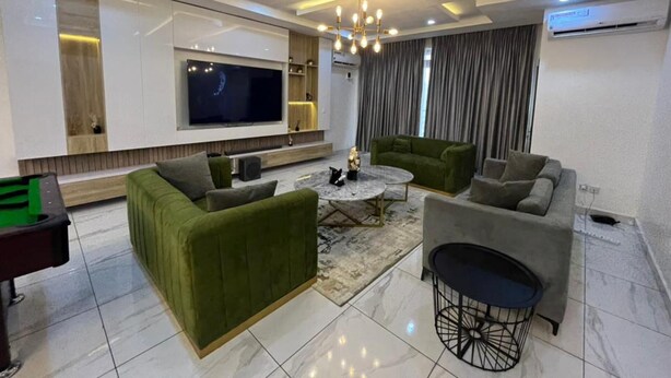 Een moderne woonkamer met een flatscreen televisie, groene banken, een bijzettafeltje en een kroonluchter.