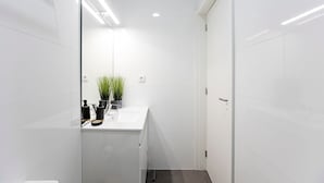 Een moderne badkamer met witte tegels, een wit wastafelmeubel en twee planten in potten op het aanrecht.