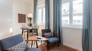 Een moderne woonkamer met een eethoek, met een ronde tafel, twee stoelen, een bank en een klein bijzettafeltje met een afstandsbediening.