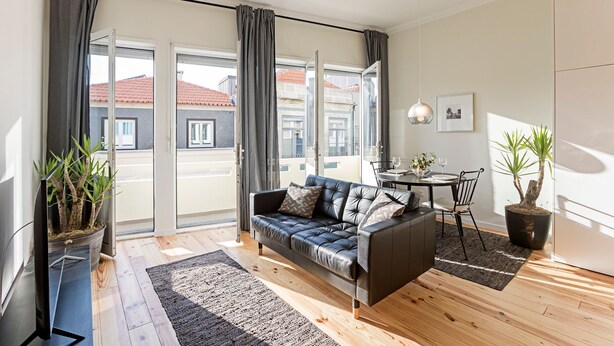 A modern living room with a leather sofa, a dining table with chairs, and a potted plant. - 150 Rivoli Apartments - 3ºA by LovelyStay (Porto)