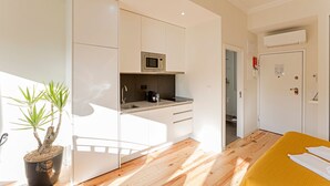 A modern kitchen with a microwave, sink, and cabinets. There is a potted plant and a yellow bed in the room. - 150 Rivoli Apartments - 3ºA by LovelyStay (Porto)