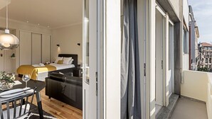 A modern hotel room with a bed, a dining area with a table and chairs, and a balcony with a view of the city. - 150 Rivoli Apartments - 3ºA by LovelyStay (Porto)