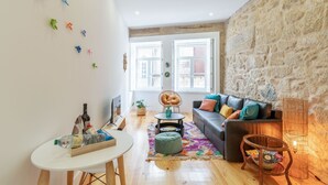 A cozy living room with a stone wall, a sofa with colorful cushions, a round table with a bottle, and a TV. - Riverside Cozy Studio by LovelyStay (Porto)