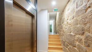 A hallway with a stone wall, a wooden staircase, and an elevator.