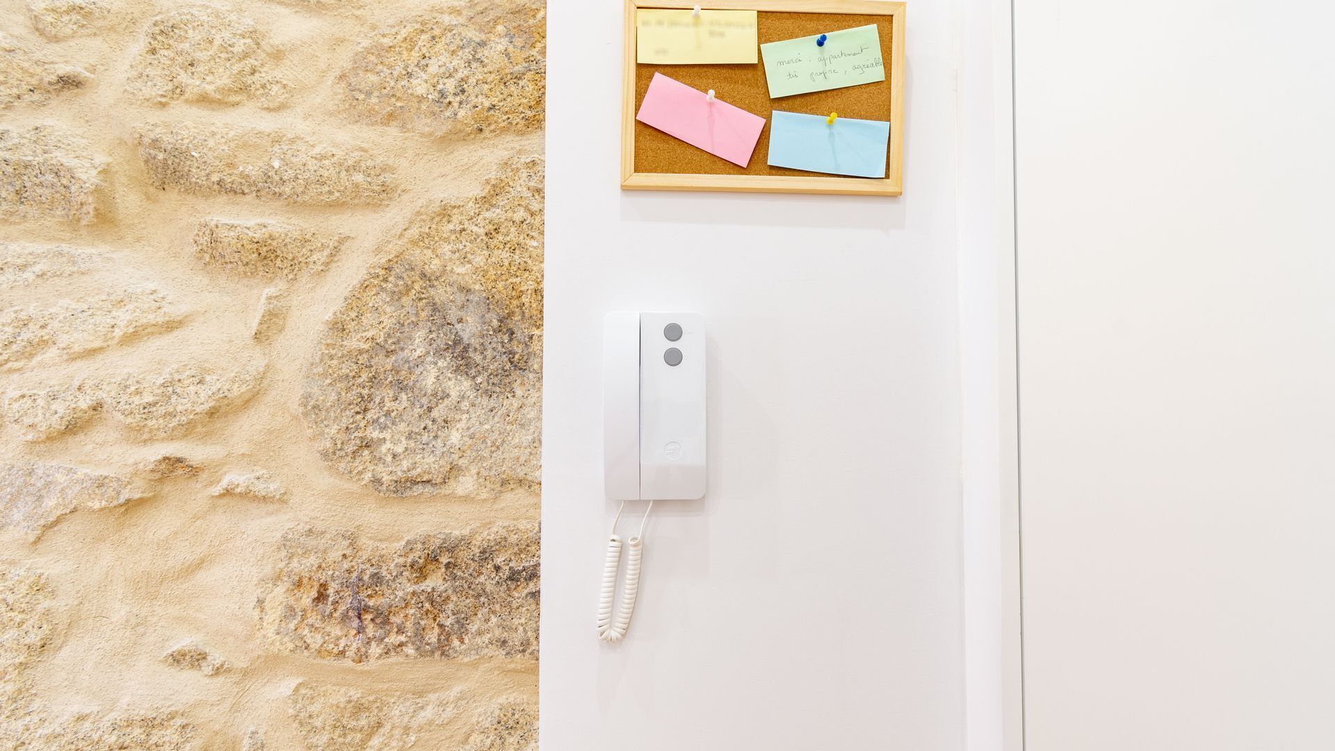 A stone wall and a corkboard with notes on a white wall.