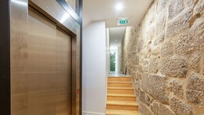 A hallway with a stone wall, a wooden staircase, and an elevator. - Riverside Cozy Studio by LovelyStay (Porto)