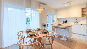 Een moderne keuken met witte kasten, een houten eettafel met vier stoelen, en een bargedeelte met krukjes.