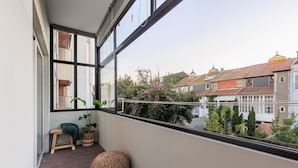Een balkon met uitzicht op omliggende huizen, een houten bankje en een plant in pot.