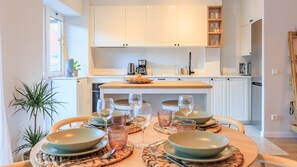 A modern kitchen with white cabinets, a wooden countertop, and a dining area set for four with plates, glasses, and cutlery.