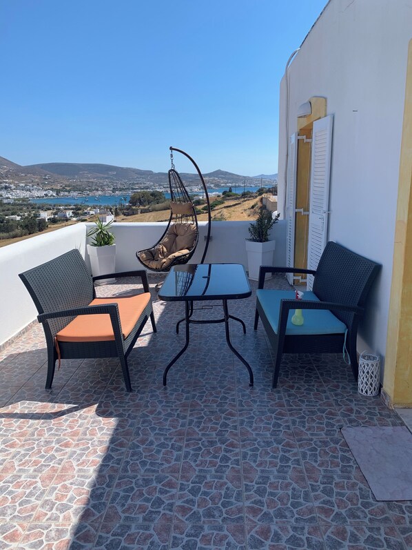 A terrace with outdoor furniture, a hanging chair, and a view of a coastal town. - Penthouse studio overlooking Paroikia Bay! (Paros)