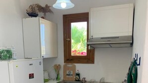 A compact kitchen with a refrigerator, microwave, sink, and a window with a view of greenery. - Penthouse studio overlooking Paroikia Bay! (Paros)