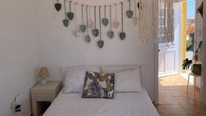 A bedroom with a bed, a nightstand, a hanging leaf decoration, and a macrame piece. - Penthouse studio overlooking Paroikia Bay! (Paros)