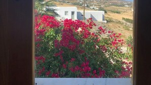 A window view of a white building with red flowers in the foreground, a clear sky, and a distant landscape. - Penthouse studio overlooking Paroikia Bay! (Paros)