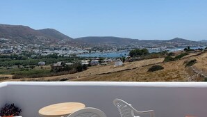 Un balcone con vista su una cittadina costiera, uno specchio d'acqua e colline in lontananza.