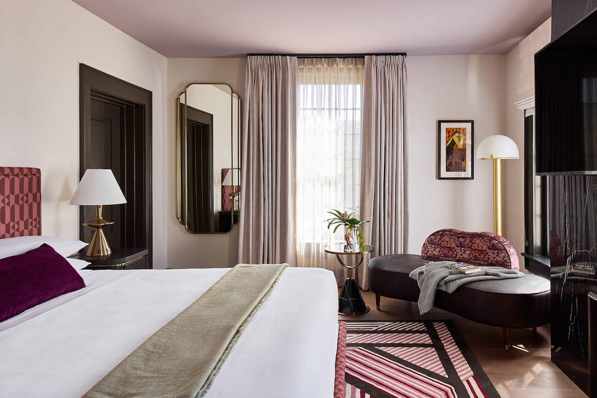 A hotel room with a large bed, a desk, a chair, a TV, and a window with curtains.