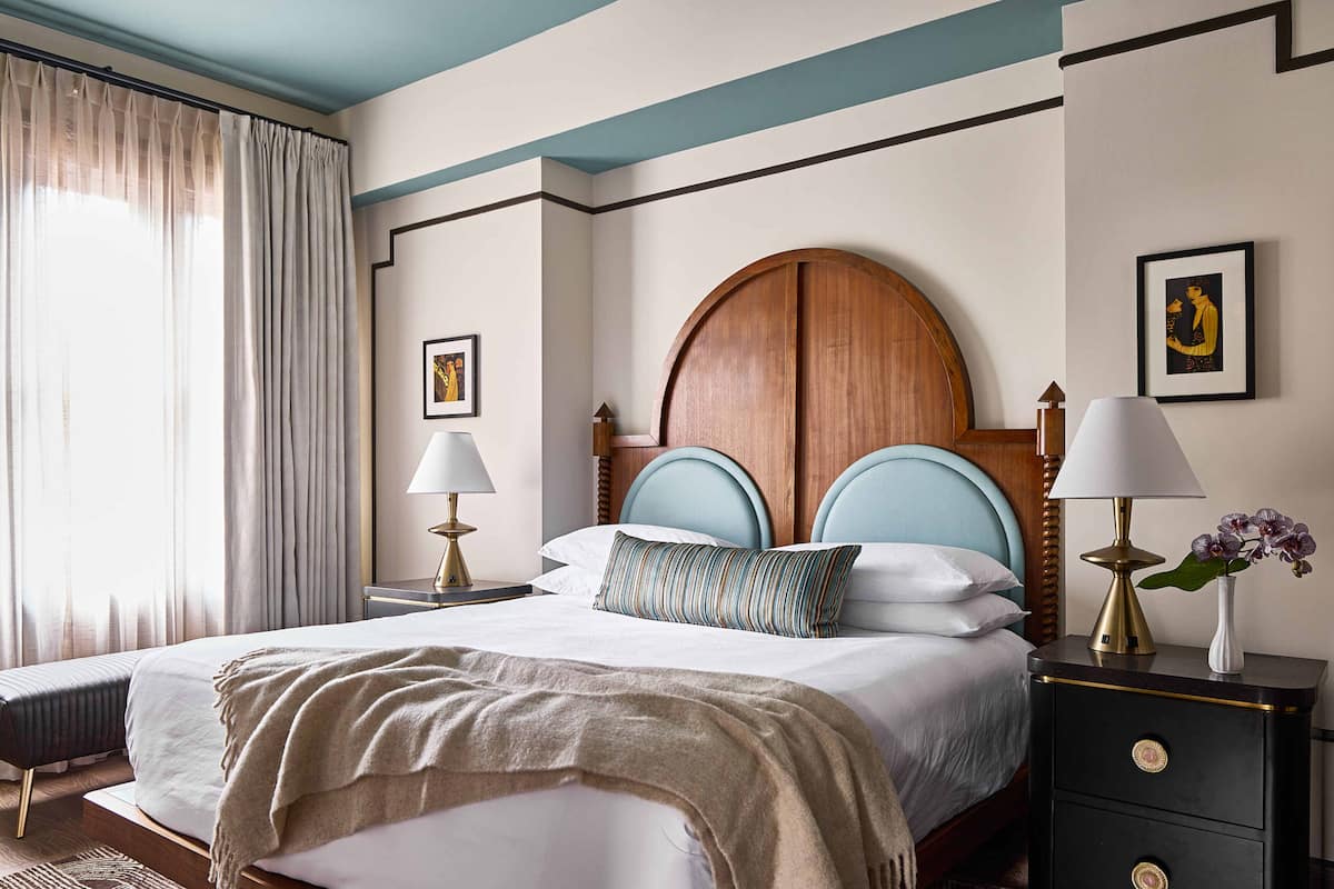 A neatly made bed with a headboard, bedside lamps, and a nightstand with a vase of flowers.