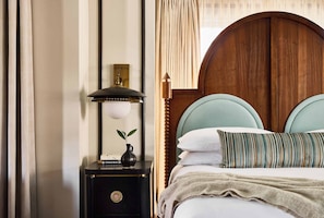 Quarto bem arrumado com cabeceira de madeira, mesa de cabeceira com abajur, um vaso com planta e almofada listrada.