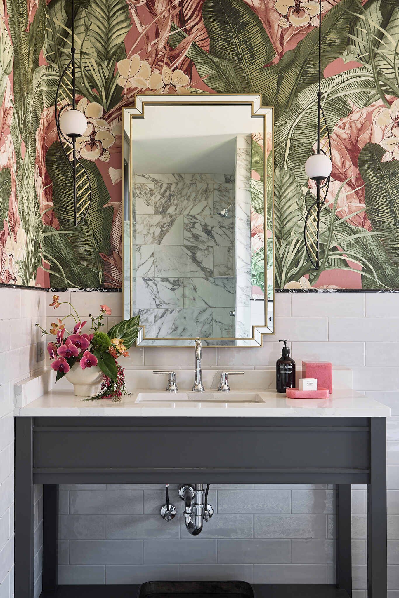 Une salle de bain avec un lavabo en marbre, un miroir avec un cadre doré et un papier peint à motifs floraux.