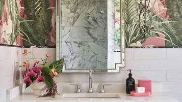 Une salle de bain avec un lavabo en marbre, un miroir avec un cadre doré et un papier peint à motifs floraux.