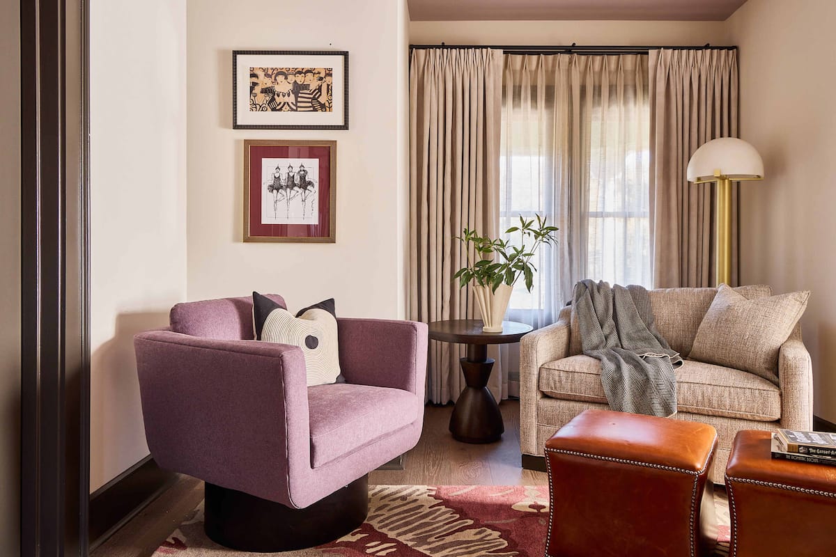 A living room with a purple armchair, a beige sofa, a small table with a plant, and a lamp.