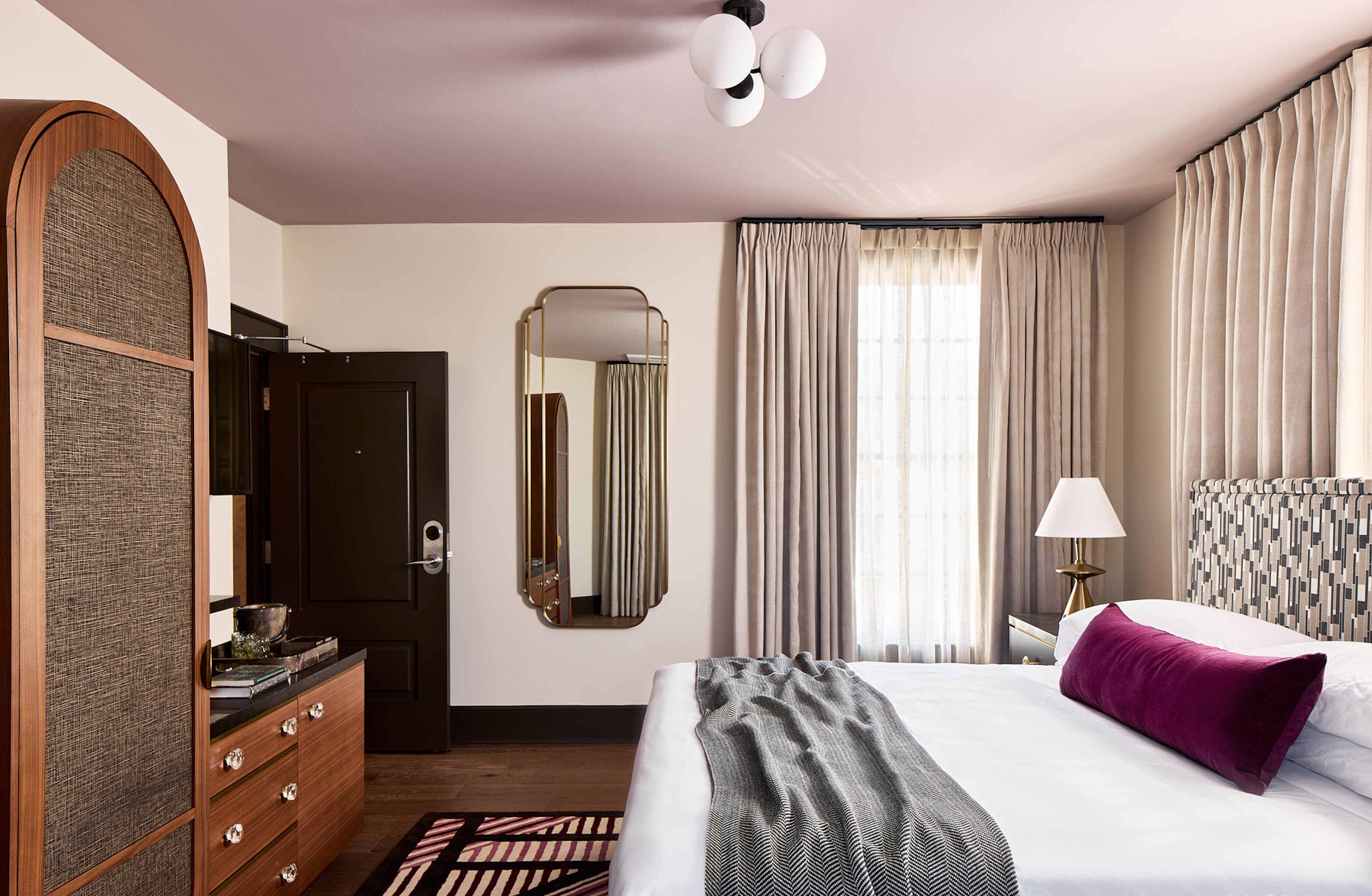 Een hotelkamer met een groot bed, een dressoir, een spiegel, een lamp en gordijnen.