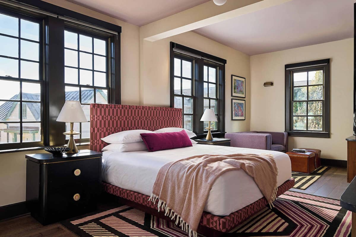A bedroom with a large bed, two bedside tables, a nightstand, a chair, and a window.