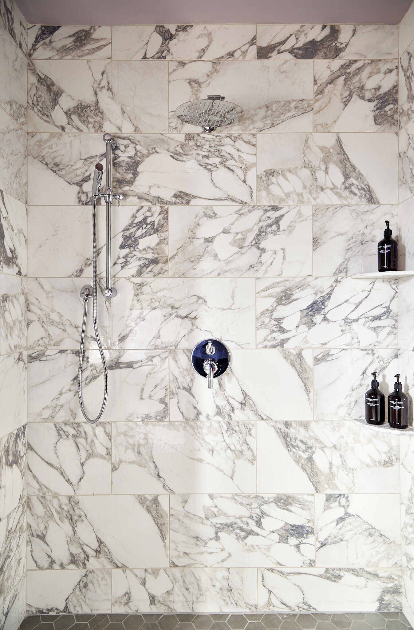 A bathroom with marble tiles, a showerhead, and two bottles on a shelf.