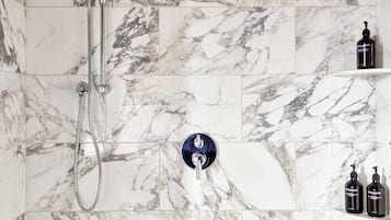 A bathroom with marble tiles, a showerhead, and two bottles on a shelf.