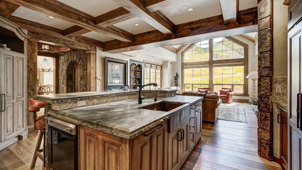A spacious kitchen with a large island, wooden beams, stone accents, and a view to the outdoors. - Golden Peak Luxury 4 BR Penthouse - Ski-in/out by RedAwning (Vail)