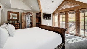 A bedroom with a large bed, wooden ceiling beams, a stone fireplace, and a view of the outdoors through large windows. - Golden Peak Luxury 4 BR Penthouse - Ski-in/out by RedAwning (Vail)