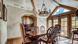 A dining area with a wooden table and chairs, a chandelier, and large windows. - Golden Peak Luxury 4 BR Penthouse - Ski-in/out by RedAwning (Vail)