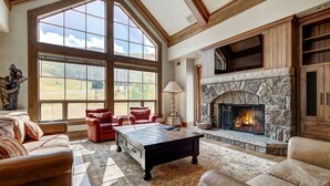 A spacious living room with large windows, a stone fireplace, leather sofas, and a coffee table. - Golden Peak Luxury 4 BR Penthouse - Ski-in/out by RedAwning (Vail)