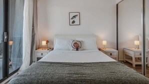 Une chambre d’hôtel avec un grand lit, deux tables de chevet avec des lampes, un tableau encadré au mur et une porte-fenêtre coulissante.
