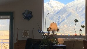 A room with a large window offering a mountain view, a star-shaped wall decoration, a lamp, and a plant on a table. - Snow Capped MTN View & Starry Nites: 1 hour to Great Sand Dunes & Monarch Skiing (Crestone)