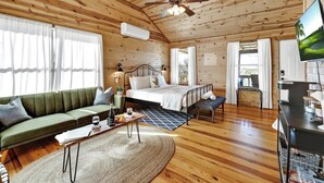 A wooden cabin interior with a bed, sofa, TV, and a dining area.