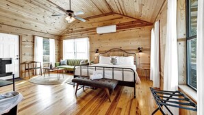 A cozy cabin interior with a wooden ceiling, a bed with a metal frame, a green sofa, and a dining area with a table and chairs.