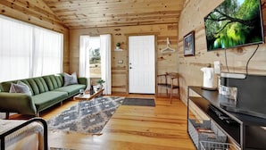A wooden cabin interior with a sofa, television, and a door leading outside.