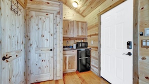 A wooden interior with a white door, a black refrigerator, and wooden cabinets.
