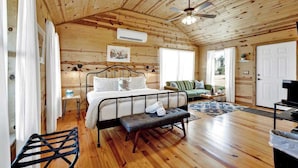 A wooden cabin interior with a bed, bench, ceiling fan, and a door.