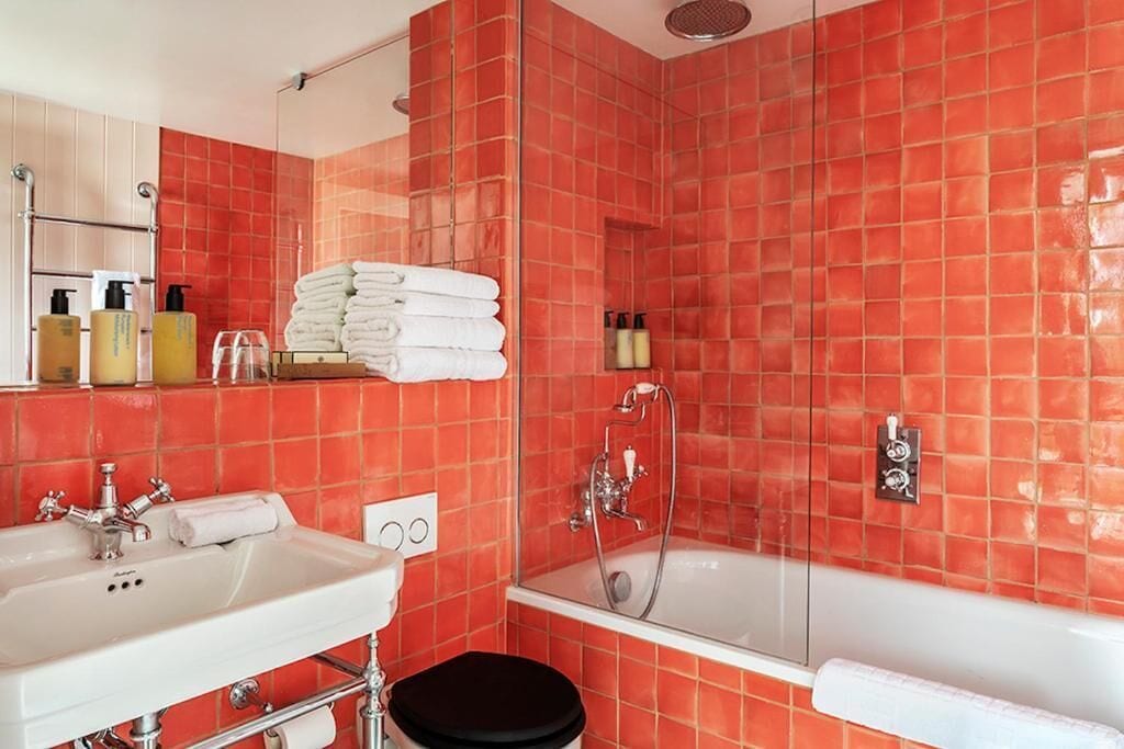 A bathroom with red tiles, a bathtub, a shower, a sink, and a toilet.