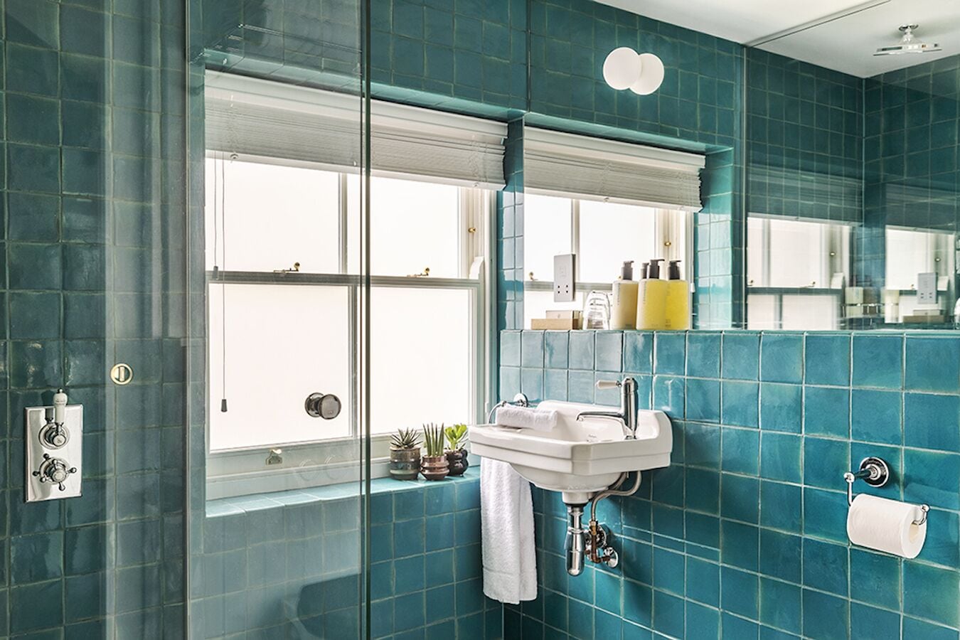 Et badeværelse med glasdør, vask med håndklæde og toiletpapirholder.