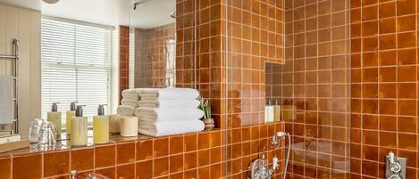 A modern bathroom with a large mirror, a bathtub, a shower area, and a vanity with toiletries.