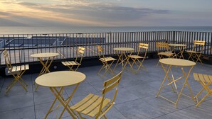 A terrace with yellow folding chairs and tables, overlooking a body of water and a dock.