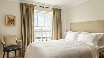 A hotel room with a large bed, a chair, a nightstand, a lamp, and a window with curtains.