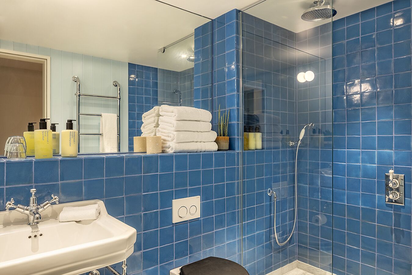 Een badkamer met blauwe tegels, een wastafel, een spiegel en een douche.